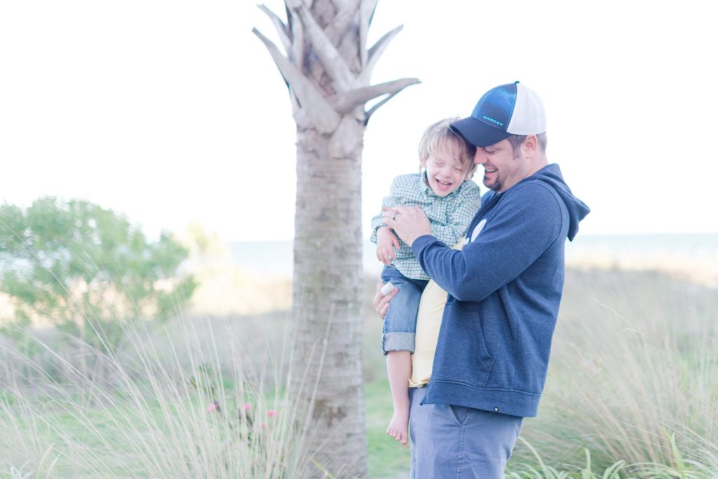 father tickling son on the beach